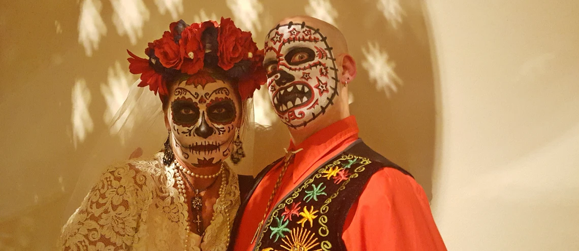 A man and a woman dressed up with their faces painted as skulls starring at the camera