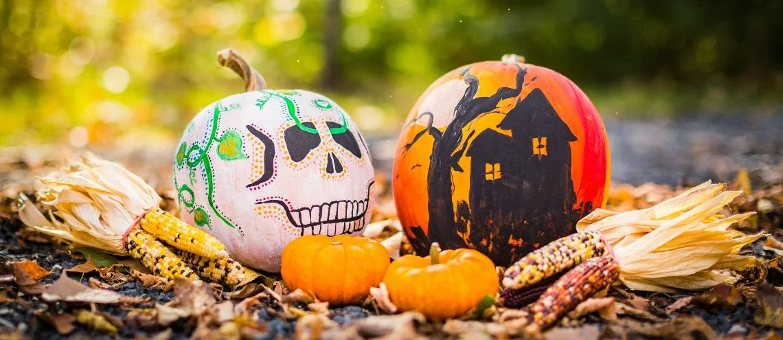 A skeleton with pumpkins and orange ball with haunted house painted on it