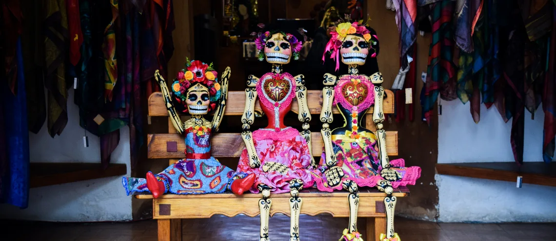 Three female skeleton models representing women in different ages sitting on a wooden bench