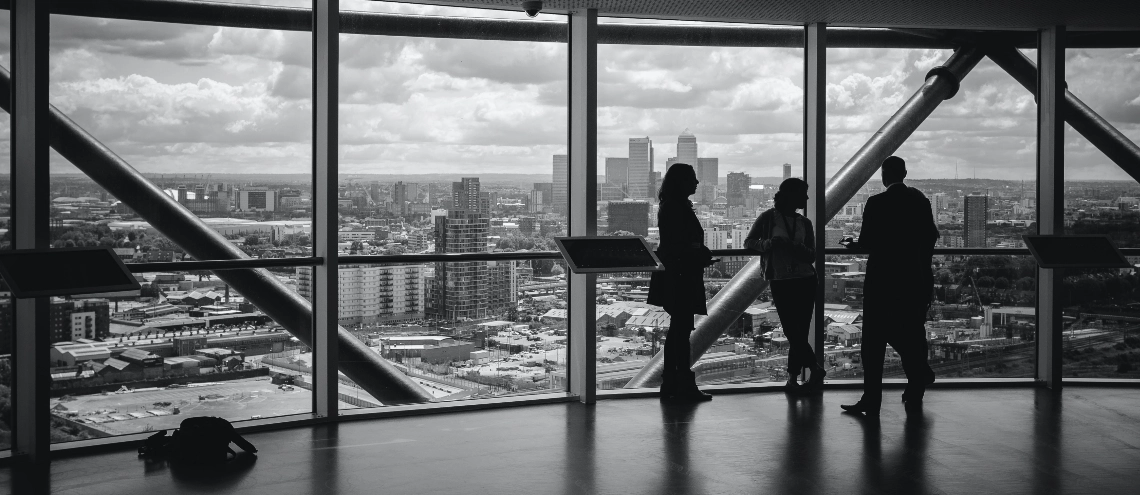 A grayscale photo of people standing inside a building overlooking a city