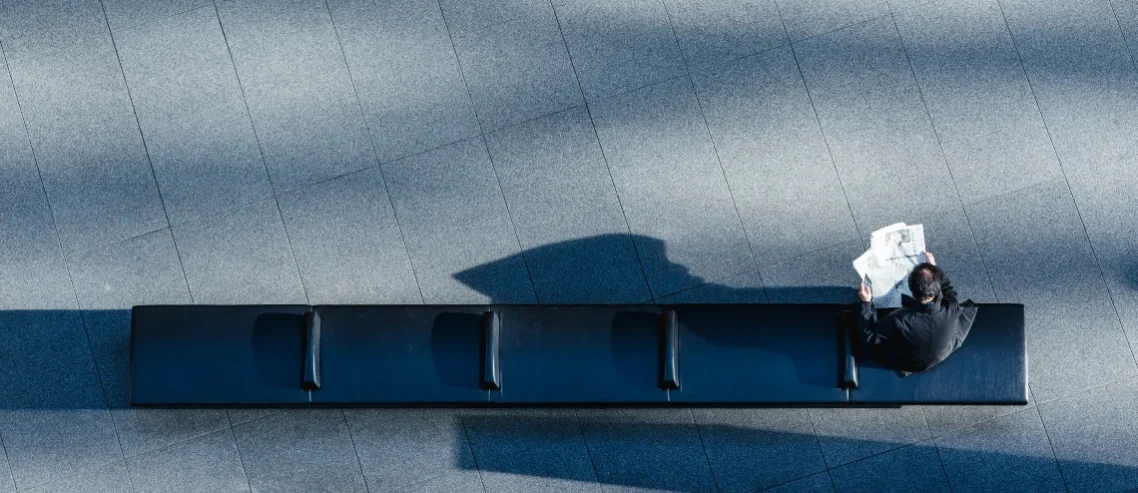 A person sitting on a black bench reading newspaper