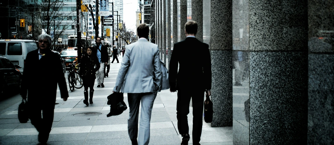 Two businesspeople walking on sidewalk pathway beside road with vehicles and high-rise buildings during daytime